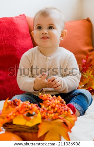 Sweet cute baby girl wearing a knitted shirt and jeans on red orange background with Autumn Fall leaves and accessories
