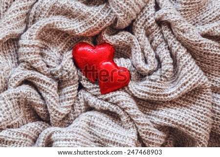 Closeup macro texture of knitted wool fabric material with red candy hearts on top, clothing background with wrinkles and folds, Valentine holiday card, love concept
