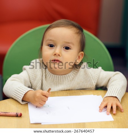 Portrait of Caucasian boy toddler sitting at the table and drawing writing studying at school, home