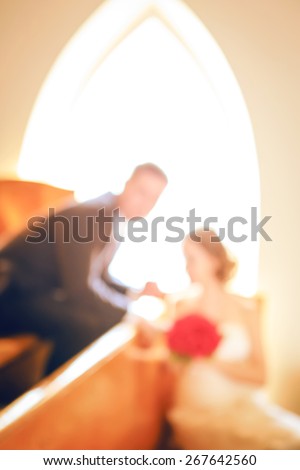 Blurry, soft, out of focus closeup portrait of smiling kissing young married couple, wedding day in church, blurry background