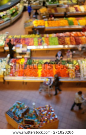 Blurred blurry soft focus background, interior of healthy food store market with fruits and vegetables, people going along the aisles and buying groceries, view from above