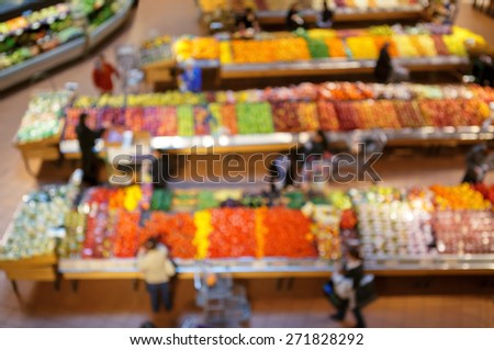 Blurred blurry soft focus background, interior of healthy food store market with fruits and vegetables, people going along the aisles and buying groceries, view from above