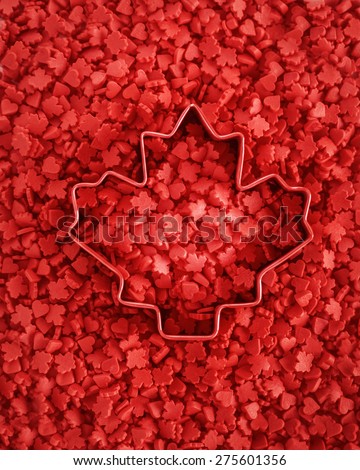 Vibrant red colorful small tiny candies maple leafs and hearts, cookie cutter with the shape of maple leaf in the center, view from above, Canada Day celebrate concept