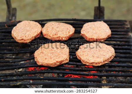 Closeup macro of five raw meat barbecue hamburgers on grill fire