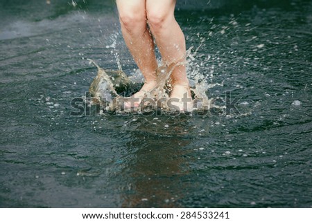 Closeup of legs feet of young girl woman jumping in puddles water during the rain, freedom, youth, childhood and happiness concept, motion blur and freeze motion effect