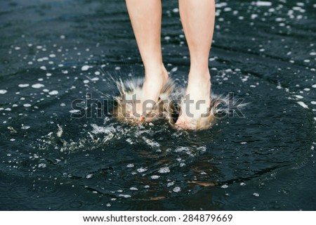 Closeup of legs feet of young girl woman jumping in puddles water during the rain, freedom, youth, childhood and happiness concept, motion blur and freeze motion effect
