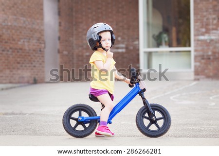 Portrait of a little girl boy toddler riding a balance bike in helmet on the road outside outdoors on a bright spring summer day, seasonal child activity concept, healthy lifestyle