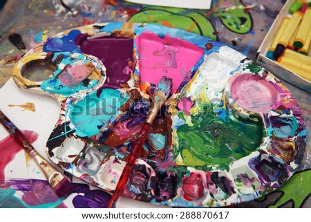 Beautiful colorful textured background, paint strokes on paper and left overs residues of paints in palette colour array on table, spots and blotches stains