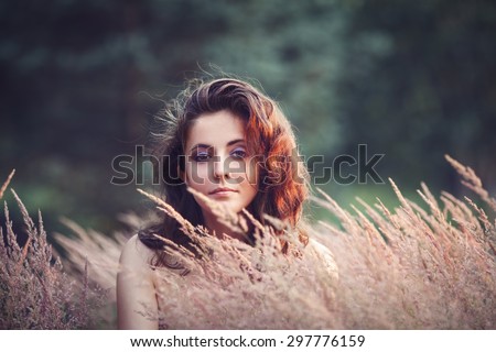 Portrait of beautiful  innocent Caucasian adult girl woman with long dark red brown hair, hazel eyes in park field outside on sunset in golden hour looking in camera