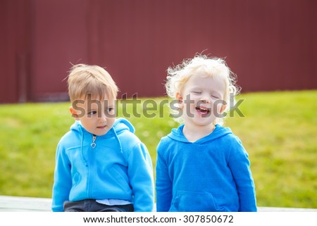 Closeup portrait of Caucasian little boy and girl friends laughing outside in park on summer day, backlit with sun from behind, rim light of his figure, selective focus, shallow depth of field