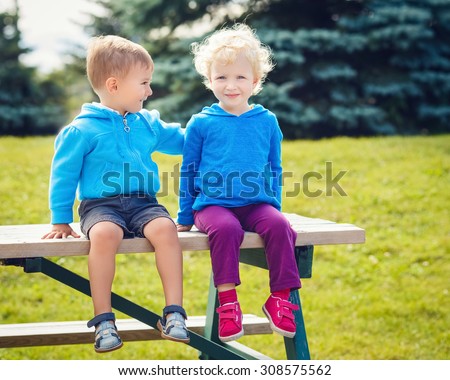 Portraits of Caucasian cute boy and girl friends laughing talking hugging outside in park on summer day, backlit with sun from behind, rim light of figures