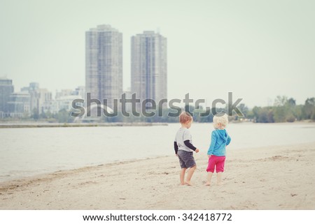 Two children boy girl walking on beach looking for something interesting  picking seashells playing together, best friends forever, toned with instagram filters retro old vintage effect, everyday life