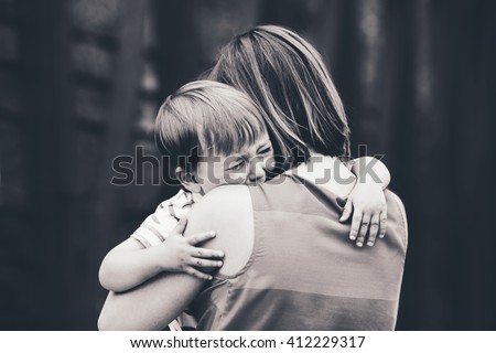 Black and white portrait of  young Caucasian woman mother comforting her crying little toddler boy son outside in park on summer day, parenthood lifestyle concept