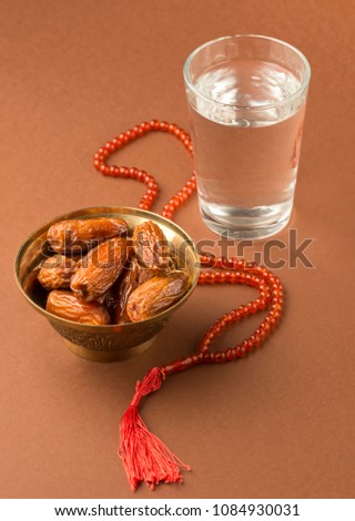 Bowl of fresh dates and glass of water with prayer beads. Beginning of meal after sunset during Ramadan.