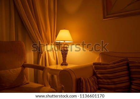 An ambient lighting in the living room. A classic decorative table lamp with shade at the side of the sofa.