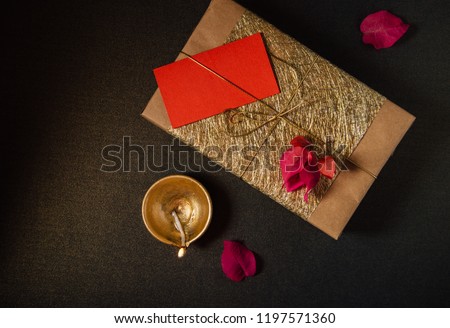 An elegant golden Indian festive gift pack and traditional terracotta lamp in dark background. View from top.