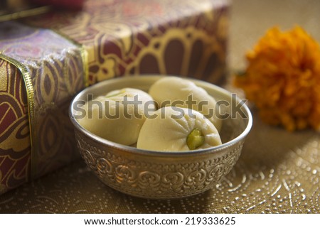 A bowl of an Indian sweet along with gift box in the background