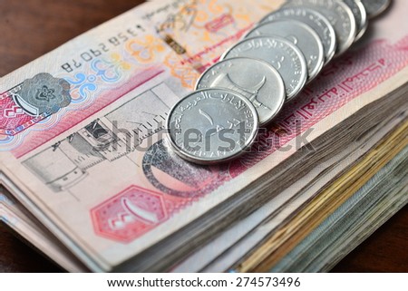many one dirham coins placed on stack of hundred dirham notes. Close up.
