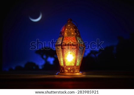 An illuminated colorful ramadan lantern against blue night sky with an crescent moon.