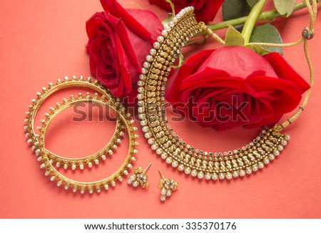 Traditional Indian gold jewelry and red roses on bright background.