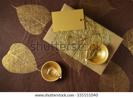 Glittering golden gift box with a blank tag and Indian traditional lamps. Diwali festive gift background. View from top.