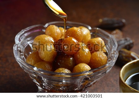 Sweet and natural date syrup is being poured on deep fried dumplings - Luqaimat. Arabic home made sweet delicacy.