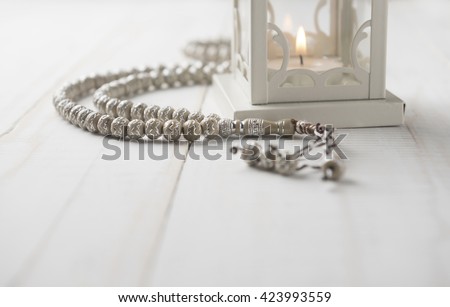 Close up of Islamic prayer beads near candle holder on white background.