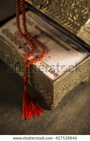 Muslim prayer beads and Saudi currency notes in vintage chest.
