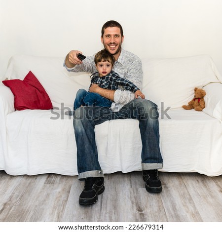 Baby and father watching tv on a white sofa