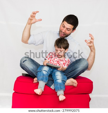Screaming father and son playing with smartphone on a red sofa - isolated on white background