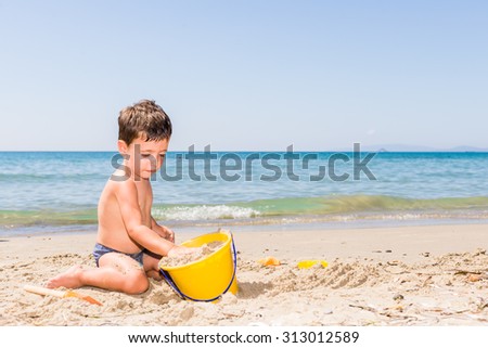 cute caucasian child playing on the beach with pail and shovel in a sunny day with sea background