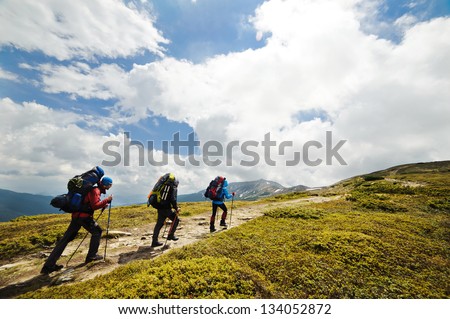 A group of people with backpacks walking along the road. There are mountains on the horizon. The sky is blue and cloudy.