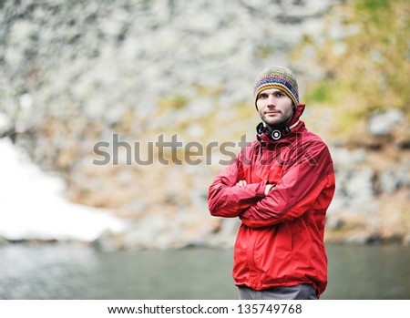 A portrait of a young happy man in front of a mountain lake.