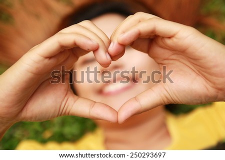 woman lies down on green grass showing hands in heart-shaped with smile mouth behind