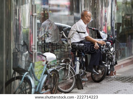 Beijing, China - August 4, 2014: An old Chinese man is smoking sitting on his motorcycle at a sidewalk in Beijing.