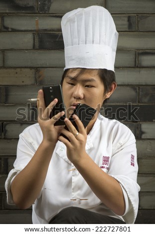 Sichuan, China - August 8, 2014: Chinese cook is checking his two phones during his break for a cigarette near the restaurant he is working in.