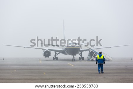 Airplane on the landing strip covered in mist. An airport worker near it.