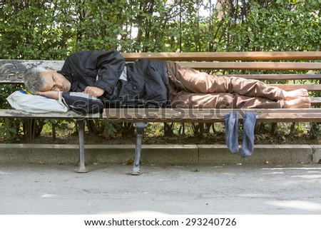 Sofia, Bulgaria - June 14, 2015: A homeless man is sleeping on a bench near Sofia\'s parliament building. Years after joining the EU Bulgaria is still struggling with great poverty among its population