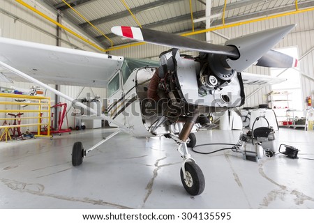 Small two-seated propeller airplane is being repaired in a hangar at the airport.