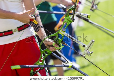 People are shooting with recurve bows during an archery competition. Hands and bows only. Green bow.