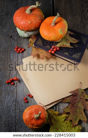 Paper with autumn leaves, pumpkin and book on wooden background. Copy space composition, selective focus