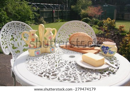 Brown Bread and Butter, on top of a bread board laid on a Garden Table, outside in a rear garden.  With oil & Vinegar jars during the summer on a sunny day