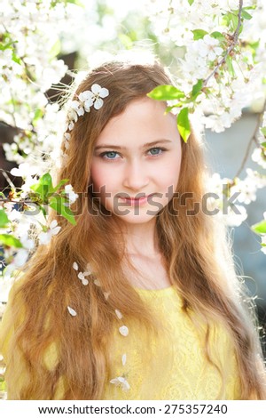 Young girl with long hairs looks ahead on a background with spring cherry trees and white flowers. Natural beauty and color.