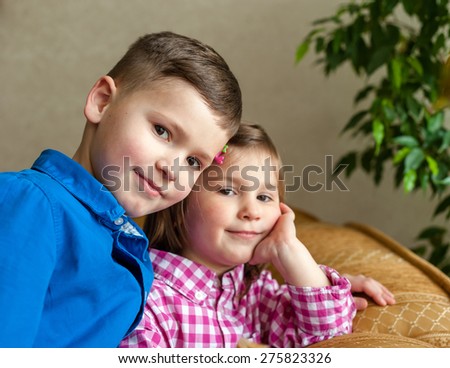 A smiling boy is an elder brother and kid sister leaned one\'s elbows on a sofa behind.