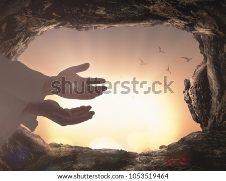 Easter Sunday concept: Silhouette Jesus Christ hands with empty tomb stone and birds flying over blurred cross on sunset background