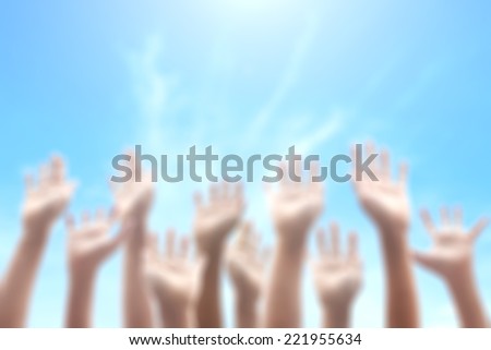 Blurred people raising hands on blue sky background