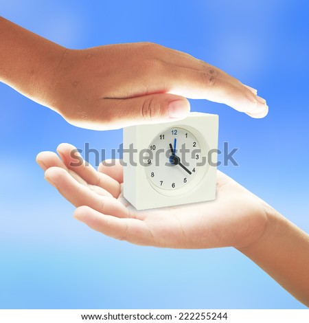Human hands save time from clock over the blue nature background.