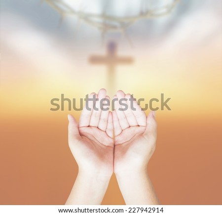 Hands of man praying over blurred crown of thorns and the cross on a sunset.