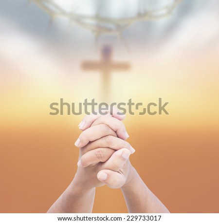 Hands of man praying over blurred crown of thorns and the cross on a sunset.