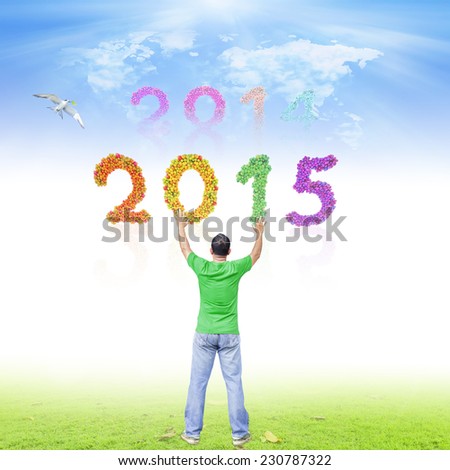 2014-2015 change represents the new year 2015. A man raising hands on meadow over fruitful text for 2014, 2015 and world map of clouds and bird have taken branches with green leaves background.